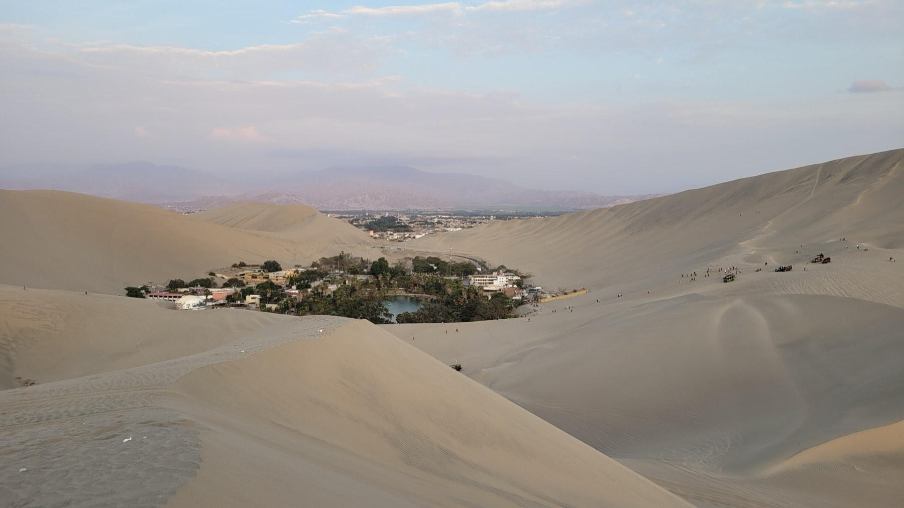 The Huacachina oasis between dunes, with the city of Ica in the distance