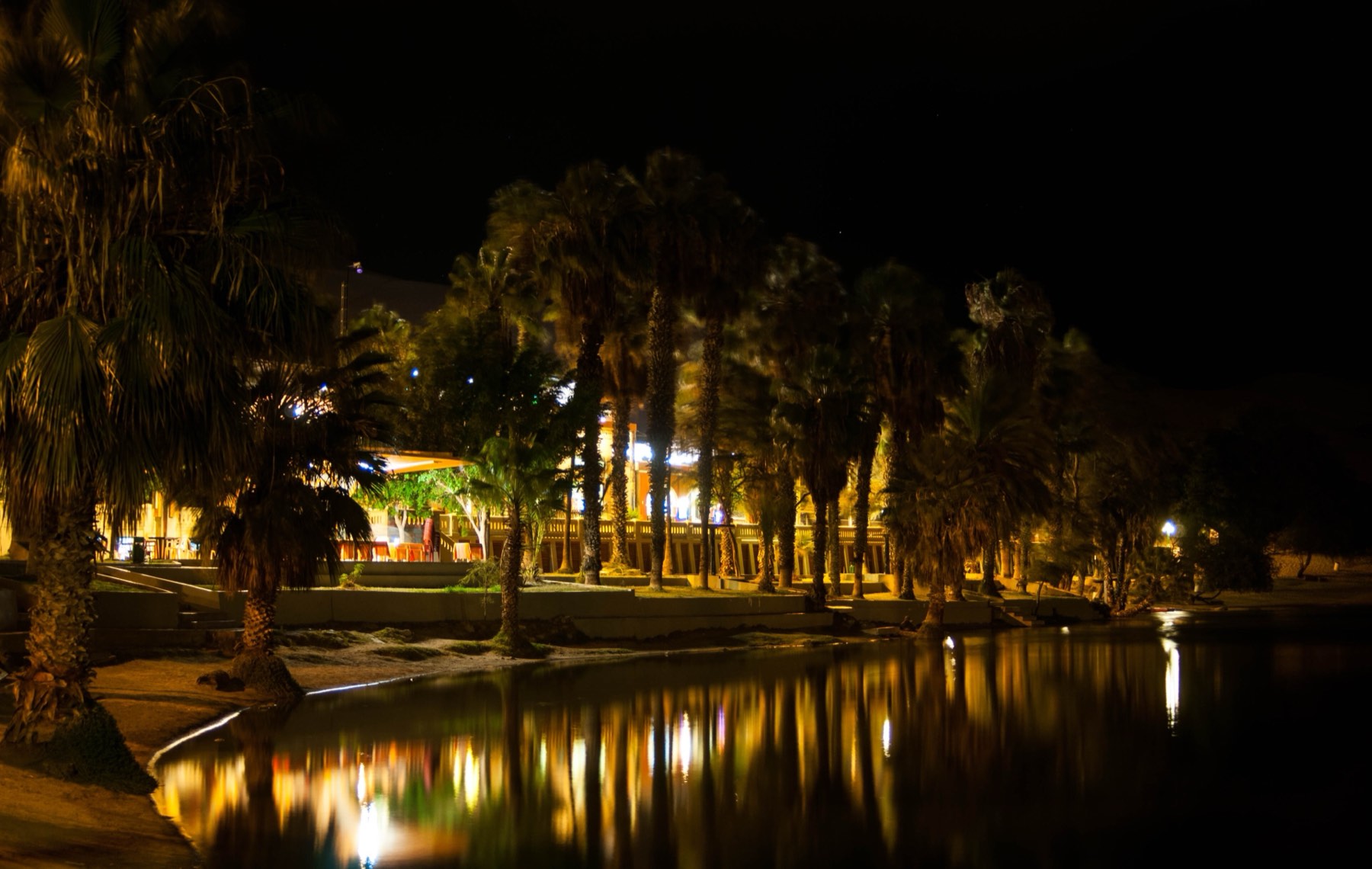 Huacachina lagoon at night, with lit palm trees reflected in the water
