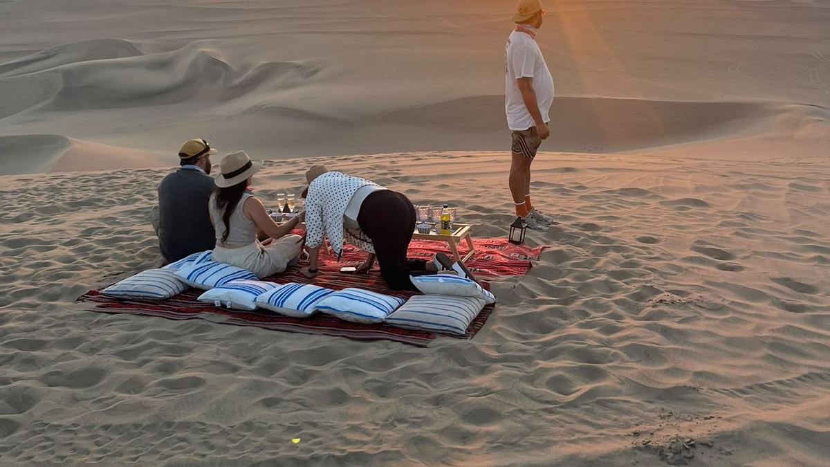 Un grupo sentado en la arena mira el atardecer sobre las dunas